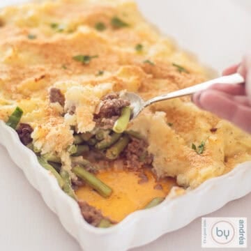 A square photo of a white baking dish, with a little bit removed from it, revealing the layers of beans, minced meat and potato puree.