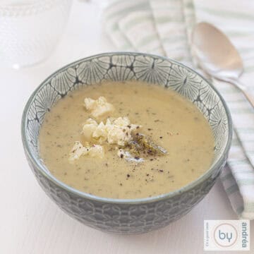 A square photo with a white background, a green bowl in the middle with courgette soup with cream, feta and pesto. A green and white tea towel is on the right.