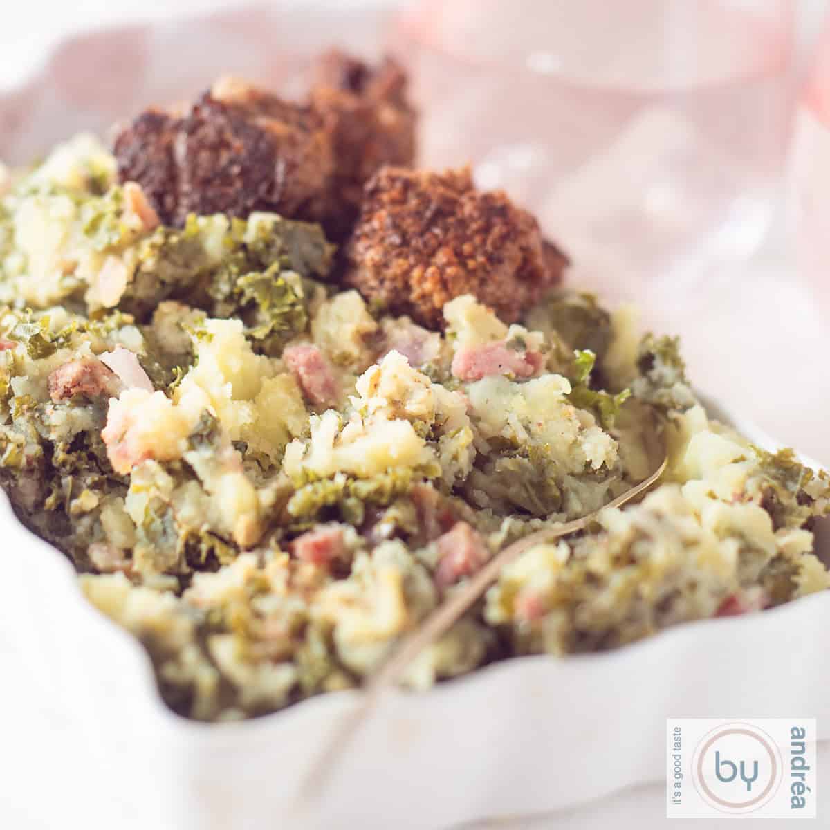 A square photo of a white bowl filled with kale mash, bacon, meatballs and gravy.