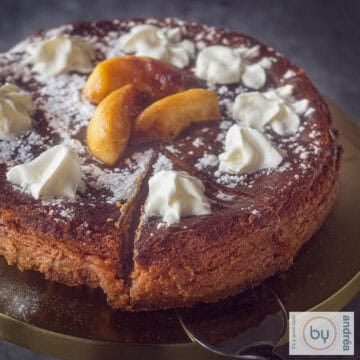 A square photo of a slice of a cheesecake with caramelized apples. Garnished with whipped cream and confectioner's sugar.