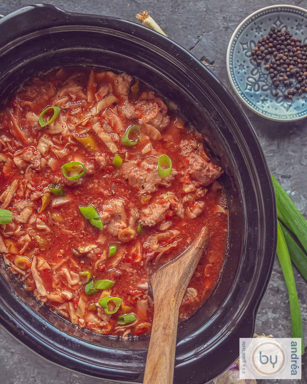 A photo from above of a slow cooker with ham steaks, cabbage and a delicious sauce on a gray background.