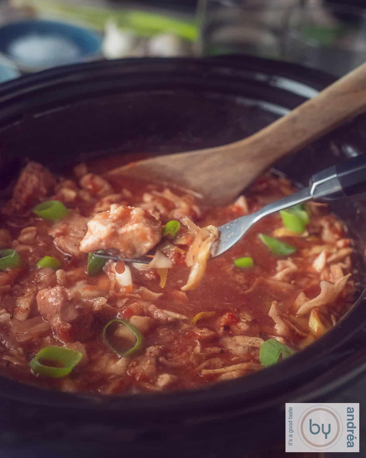A photo of part of a slow cooker filled with ham steak, cabbage and a rich sauce. A fork scoops some out of the slow cooker