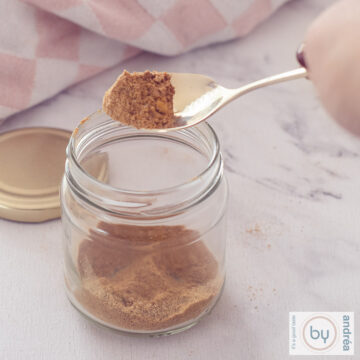 A square photo of a glass jar filled with nasi spices. A spoon scoops spices out of the jar.