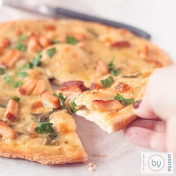 A square photo of a pizza alfredo with a hand taking a slice.
