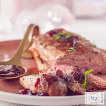 A square picture with fried duck breast with cranberry sauce on a pink plate