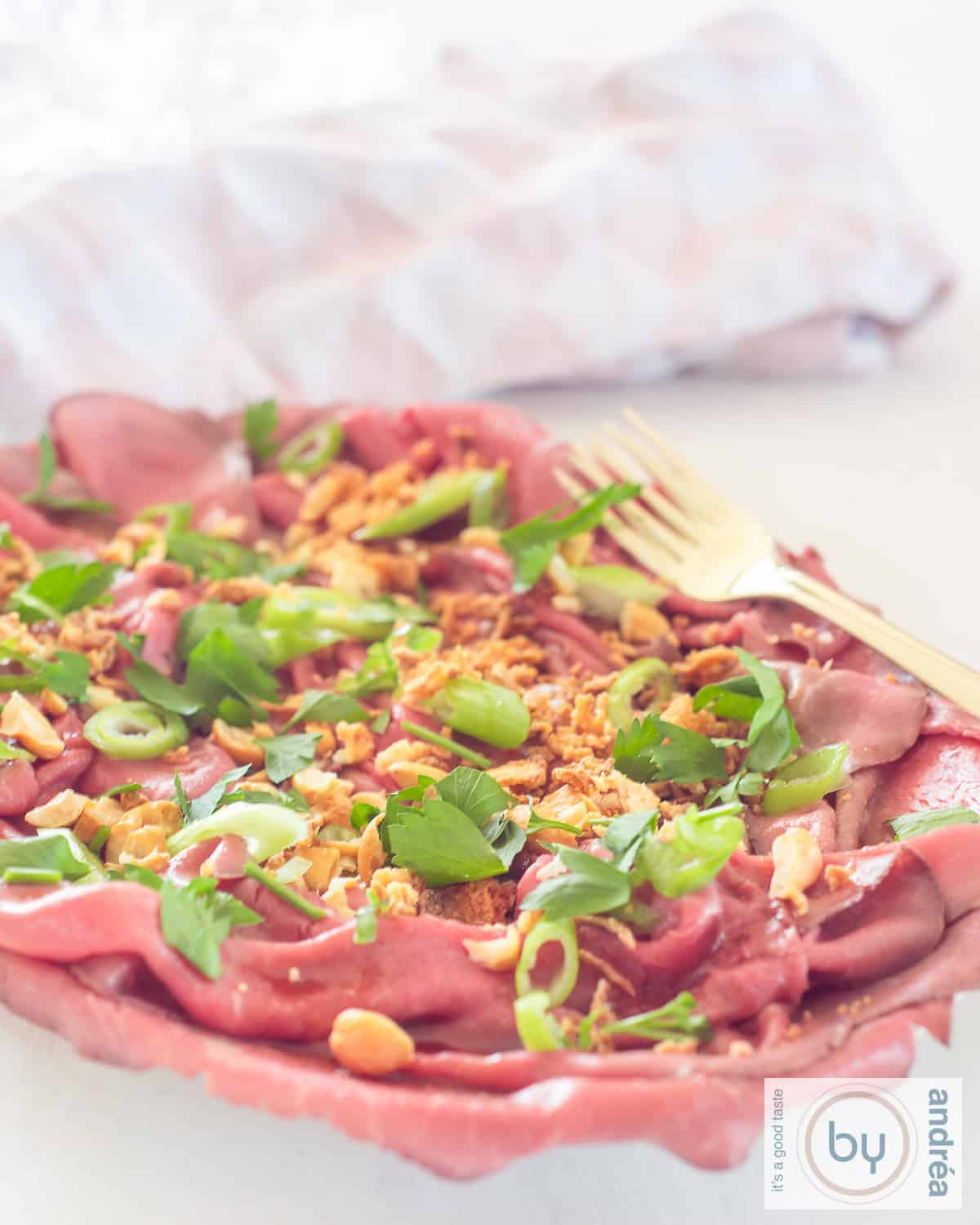An aerial photo of a bowl of roast beef salad with spring onion, Asian dressing, cashew nuts and onions