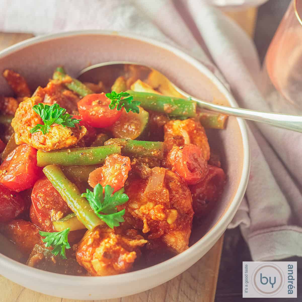A square photo with a pink bowl with chicken cubes, beans, tomatoes and zucchini in a spicy sauce.
