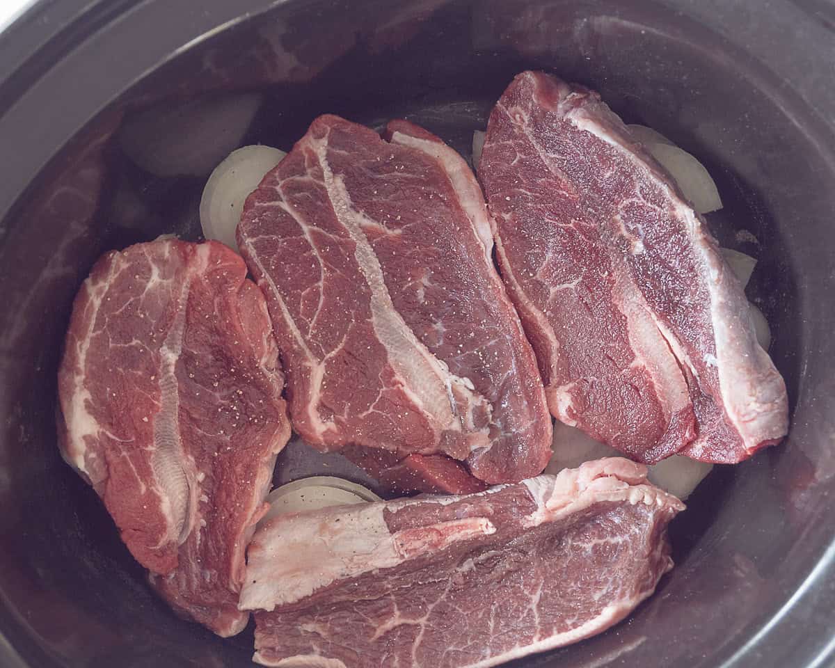 A layer of onion with garlic and then blade steaks in the slow cooker