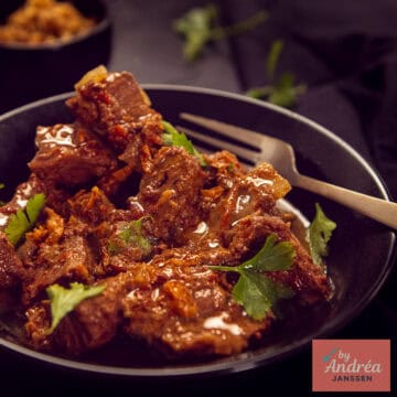 A square picture with a black plate filled with slow cooker curry madras, homemade.
