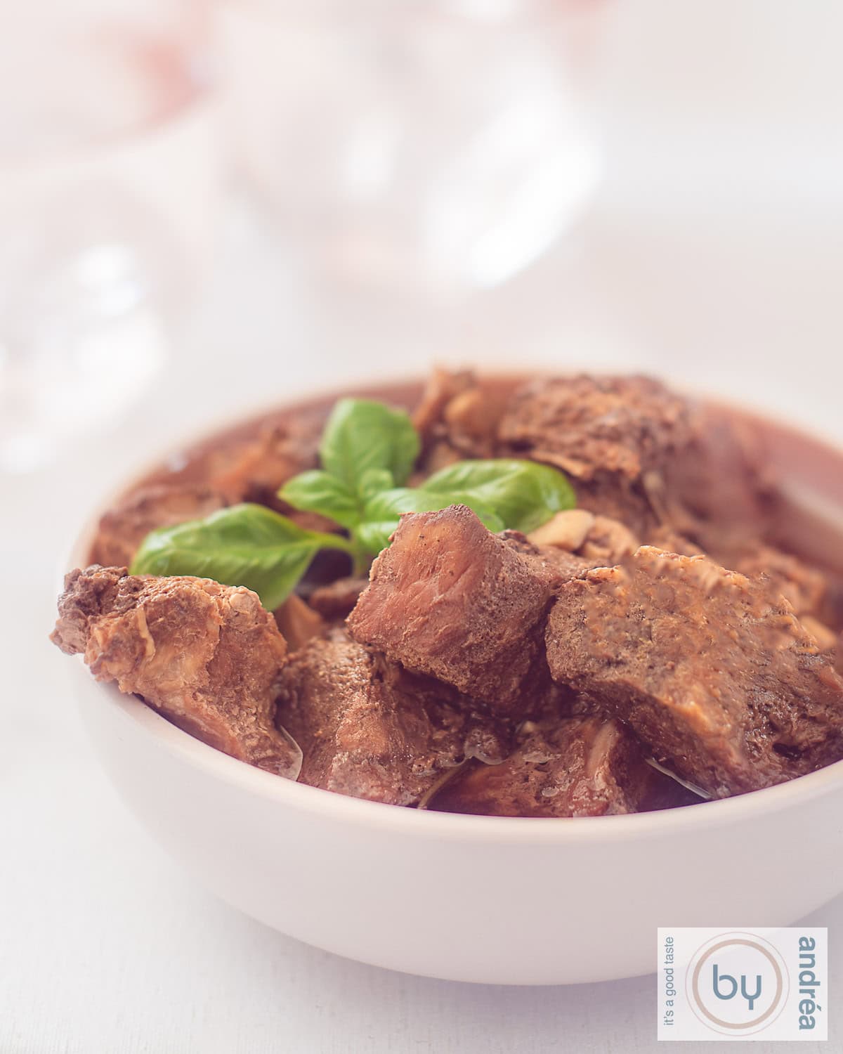 A height photo of a pink bowl filled with peposo and a sprig of basil
