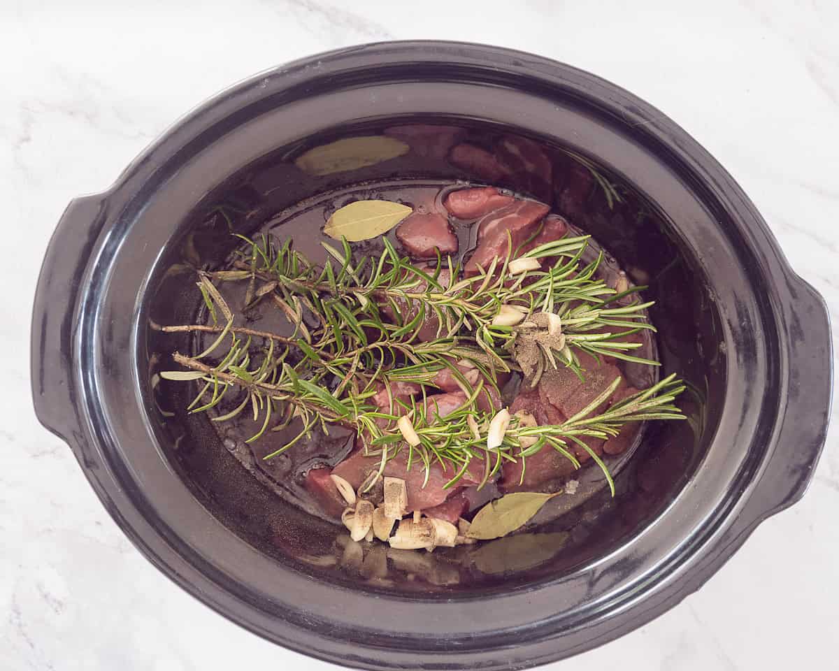 Slow cooker filled with meat, wine, herbs and seasonings.
