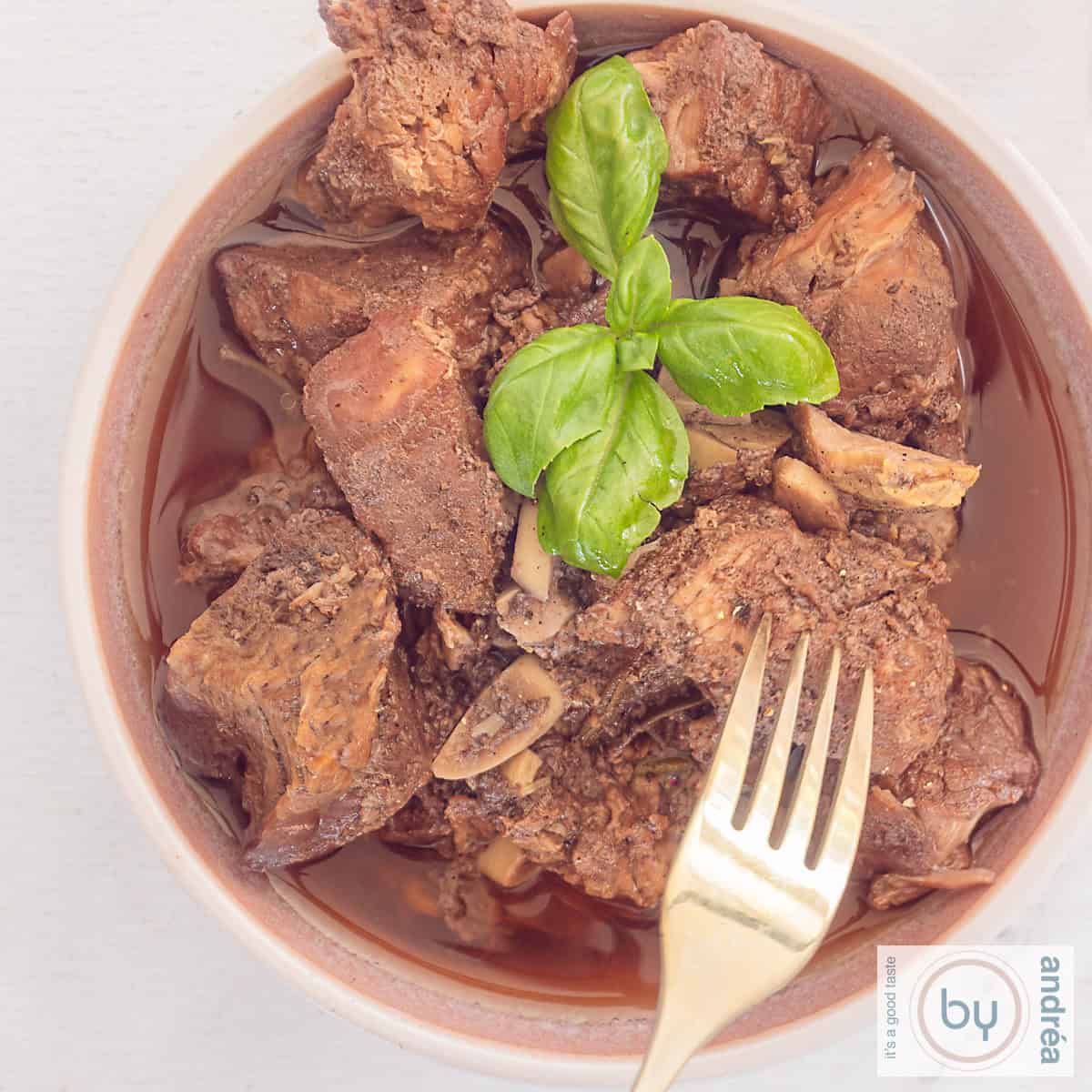 A square photo of a pink bowl of peposo stew. A fork pokes the tender meat