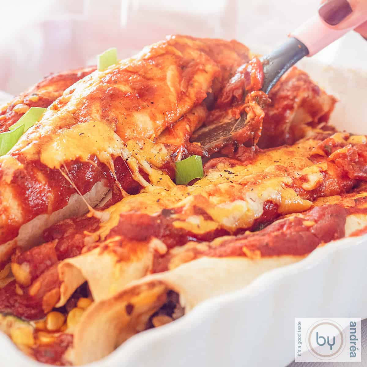 A square photo of a white bowl with Mexican enchiladas filled with ground beef, corn, tomato sauce and cheese.