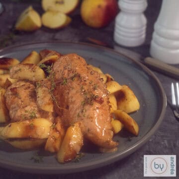 A square photo with a gray plate with chicken fillet with sauce and apples.