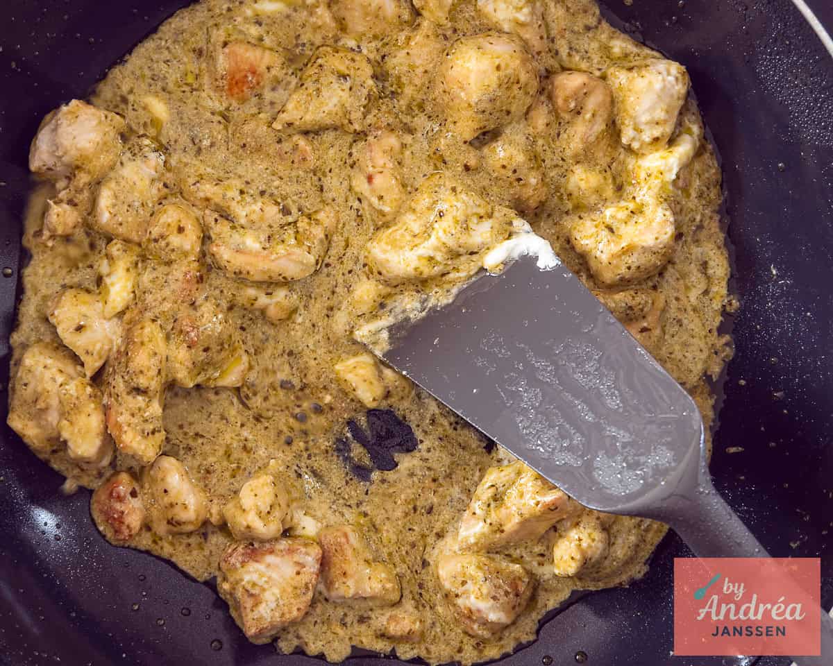 A pan of chicken cubes in a creamy pesto sauce