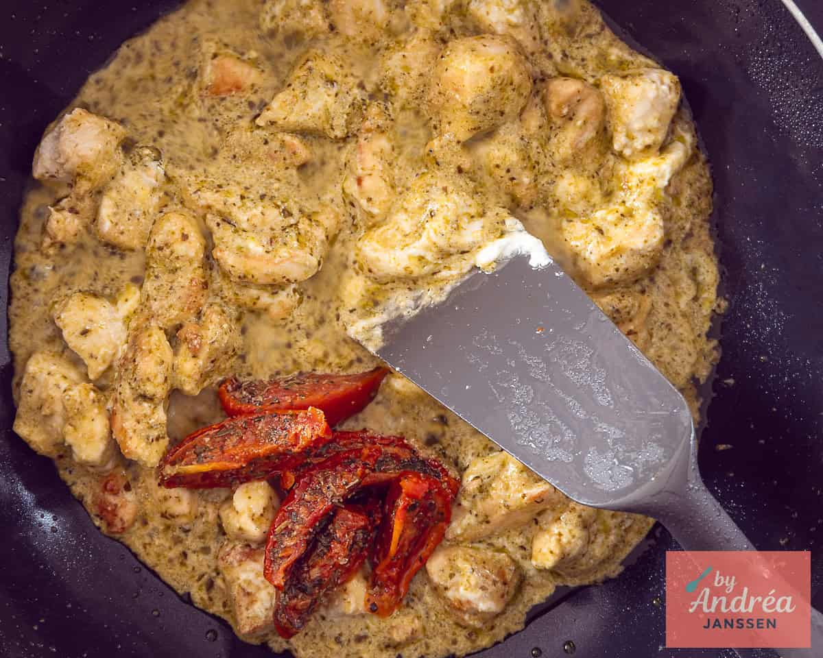 A sauté pan with chicken, creamy pesto sauce, and sun-dried tomatoes