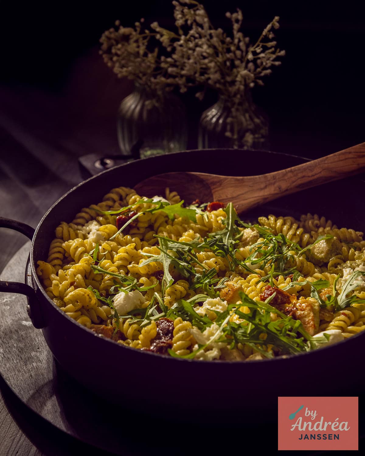 A black casserole filled with fusilli, chicken, arugula, sun-dried tomatoes, and a creamy pesto sauce.