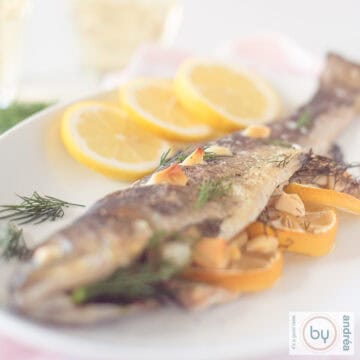A square photo of a white plate with oven-baked salmon trout filled with lemon, dill and garlic.