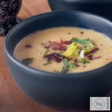 A square photo of a dark gray bowl of Groningen mustard soup with leek and bacon.