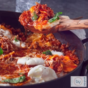 A square photo of a skillet with lasagnette. A wooden spoon holds up some lasagnette.
