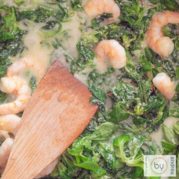 A square photo with lamb's lettuce, creamy sauce, shrimps and a wooden spoon.