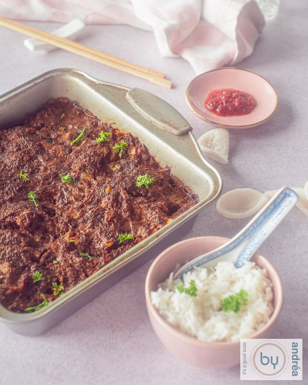 An height photo with a bowl of frikadel pan, a small bowl of rice and a pink plate with sambal.