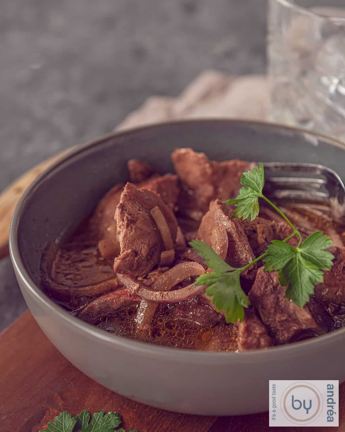 A grey bowl with cubes of entrecote, onion and a delicious sauce. Garnished with parsley.