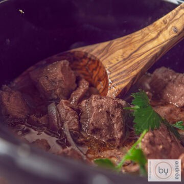 A square photo showing part of a slow cooker containing entrecote with butter sauce.