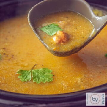 A square photo of a slow cooker filled with creamy filled vegetable soup with meatballs