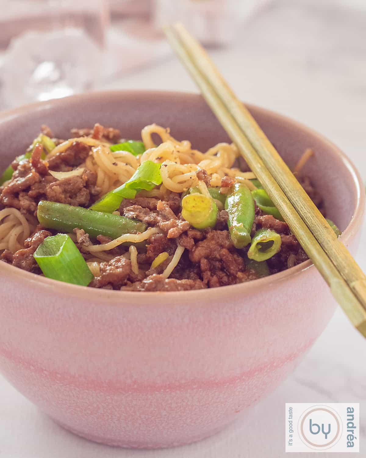 A height photo of a pink bowl of noodles with minced meat and beans.