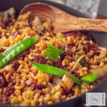 A pan filled with macaroni with an Indonesian twist, minced meat and vegetables. A wooden spoon lies in the pan.