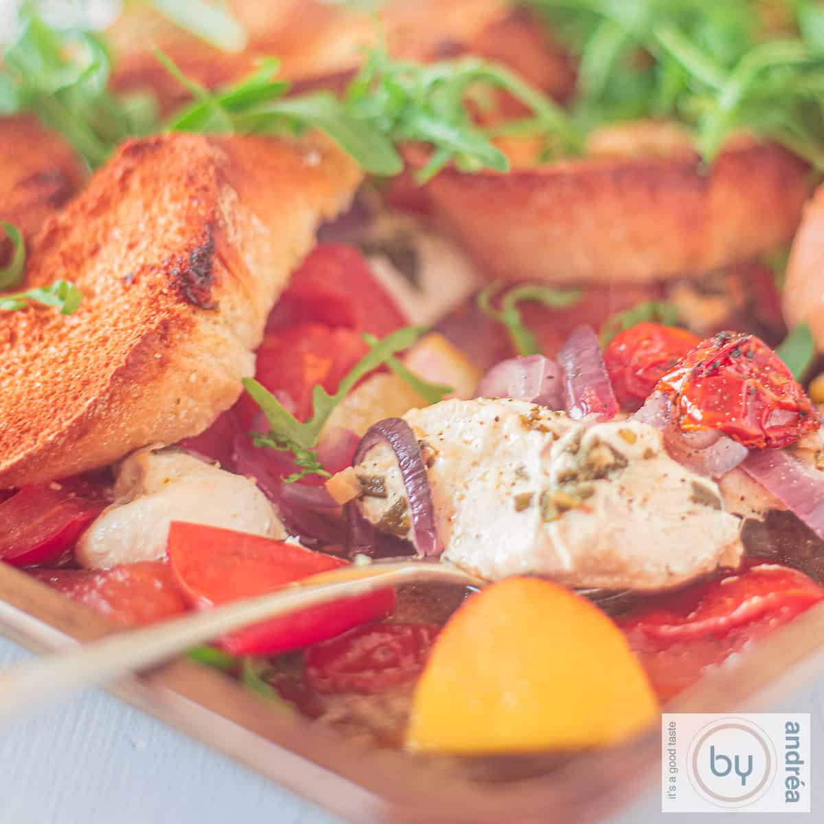 A square photo of an Italian casserole with lemon, tomato, and arugula