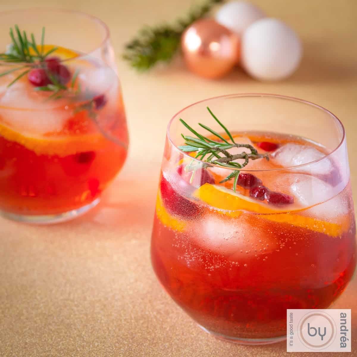 Vierkante foto van twee glazen kerstpunch met sinaasappel en rozemarijn.