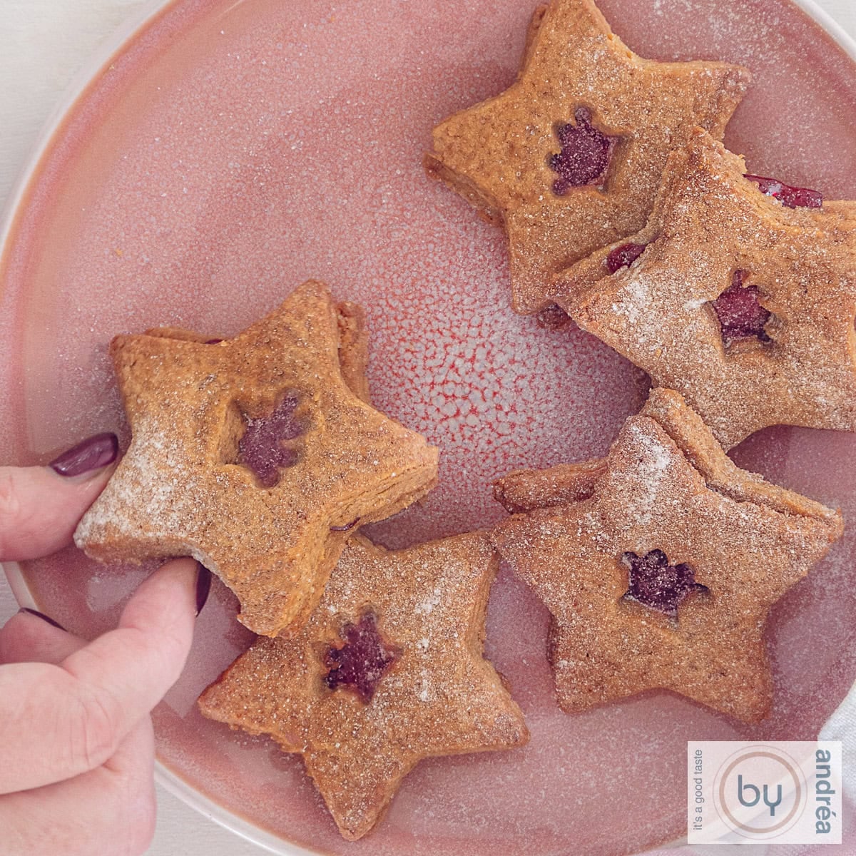 Een vierkante foto met kerstkoekjes met jam op een roze bord.