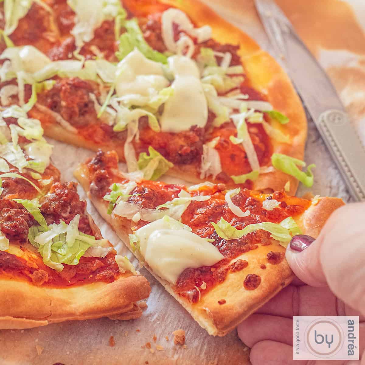 A square photo of a slice of pizza. A hand takes away a slice.