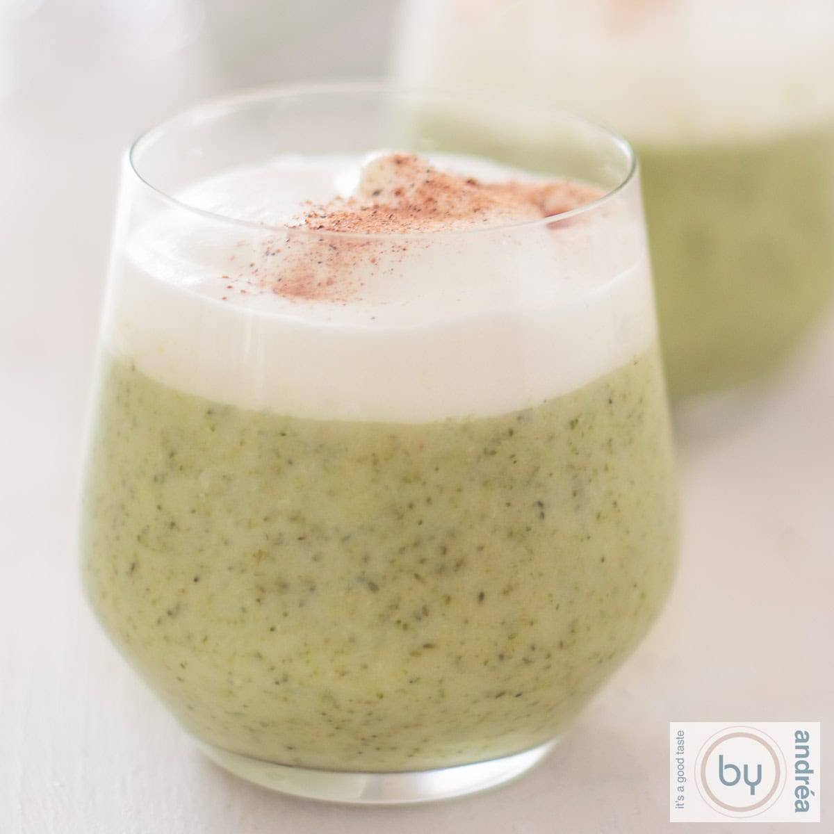 Een vierkante foto met in het midden een glas gevuld met broccolisoep met een romige toplaag.