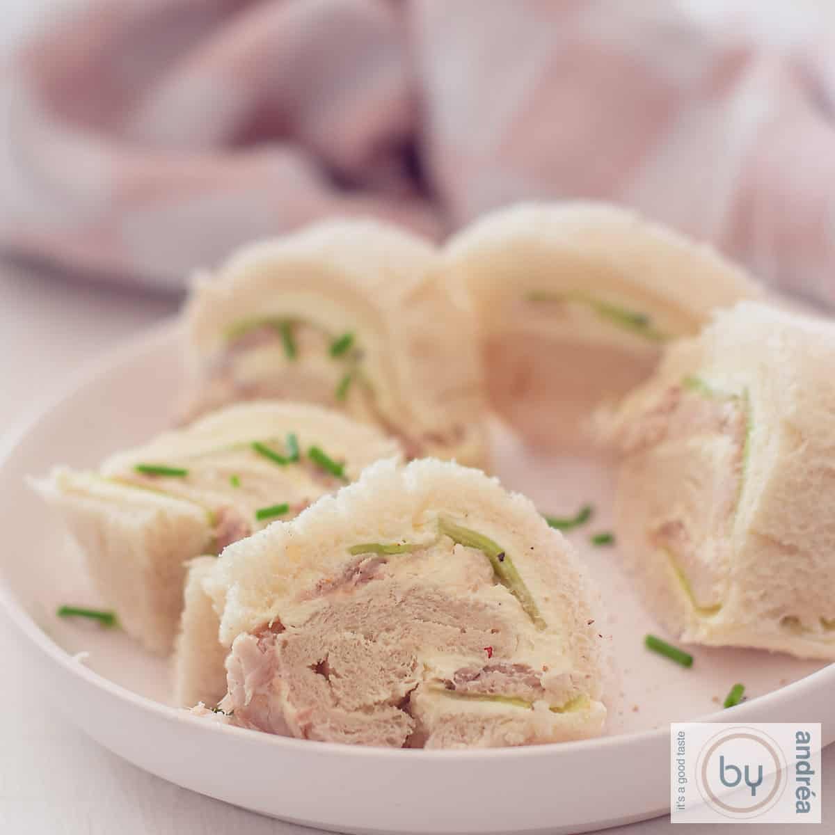 Een vierkante foto met een broodrolletje met gerookte makreel en komkommer