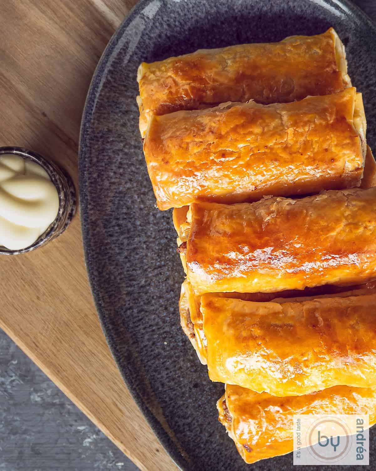 Top view photo of a gray tray with a stack of sausage rolls and a bowl of mayo