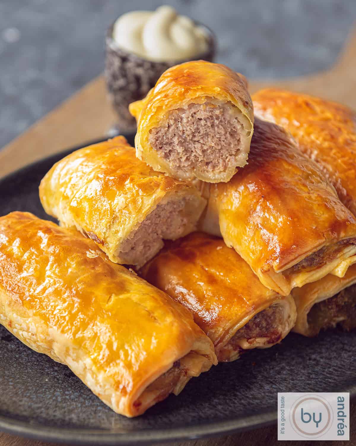 A tray of sausage rolls, the top one halved, minced meat filling visible