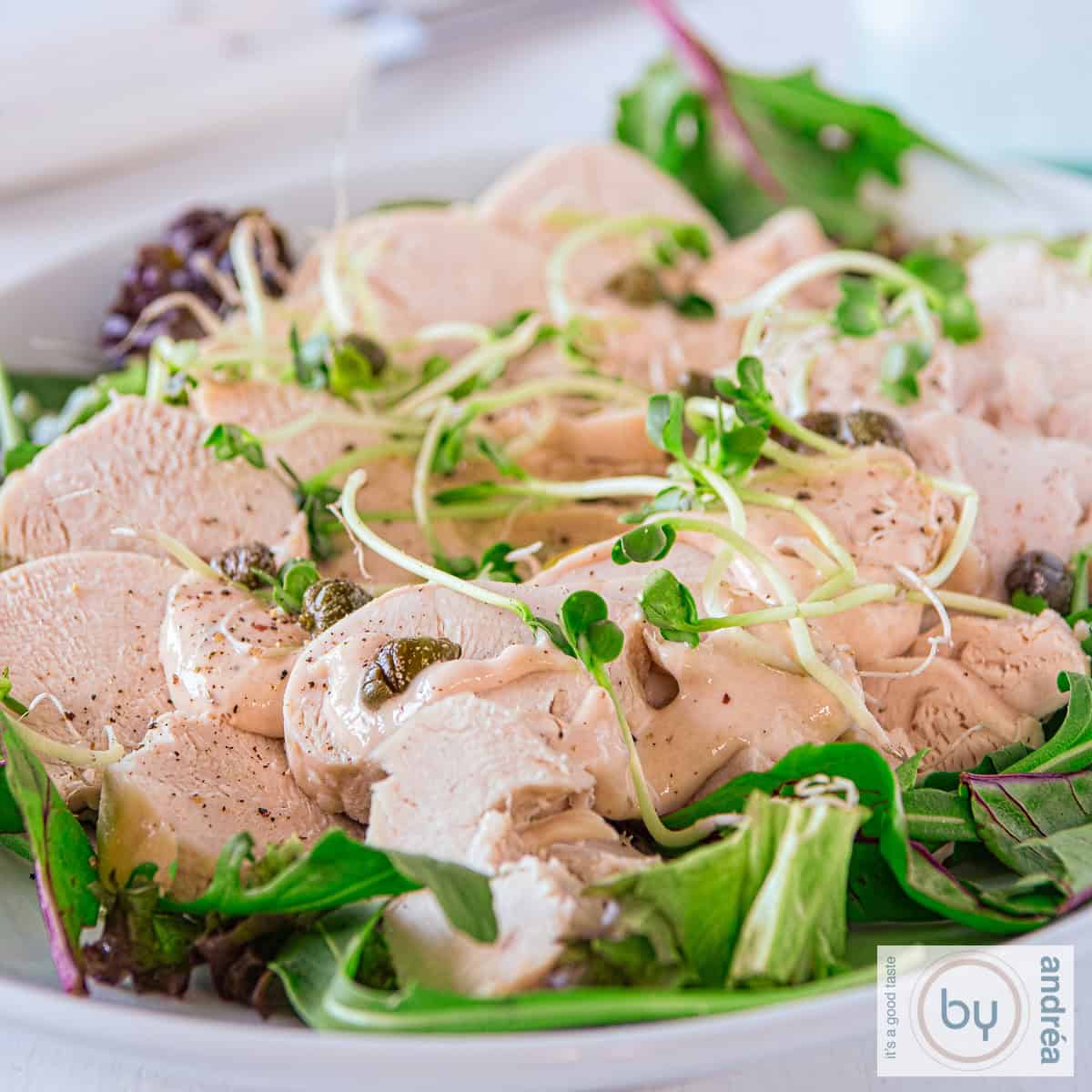 Een vierkante foto met kalkoen vitello tonnato op een bedje van sla