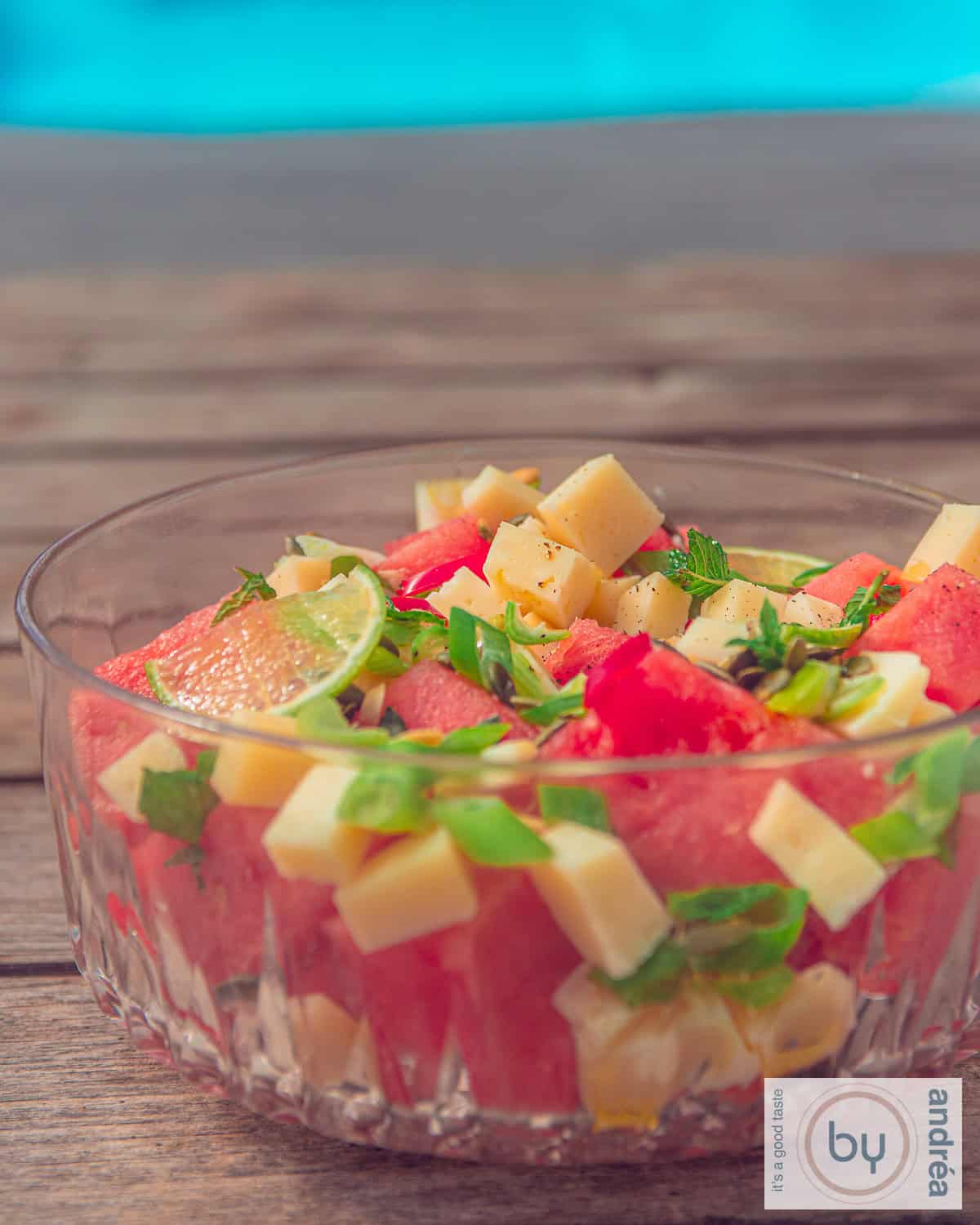 A glass bowl with goat cheese cubes, watermelon, spring onion and lime. A summer salad