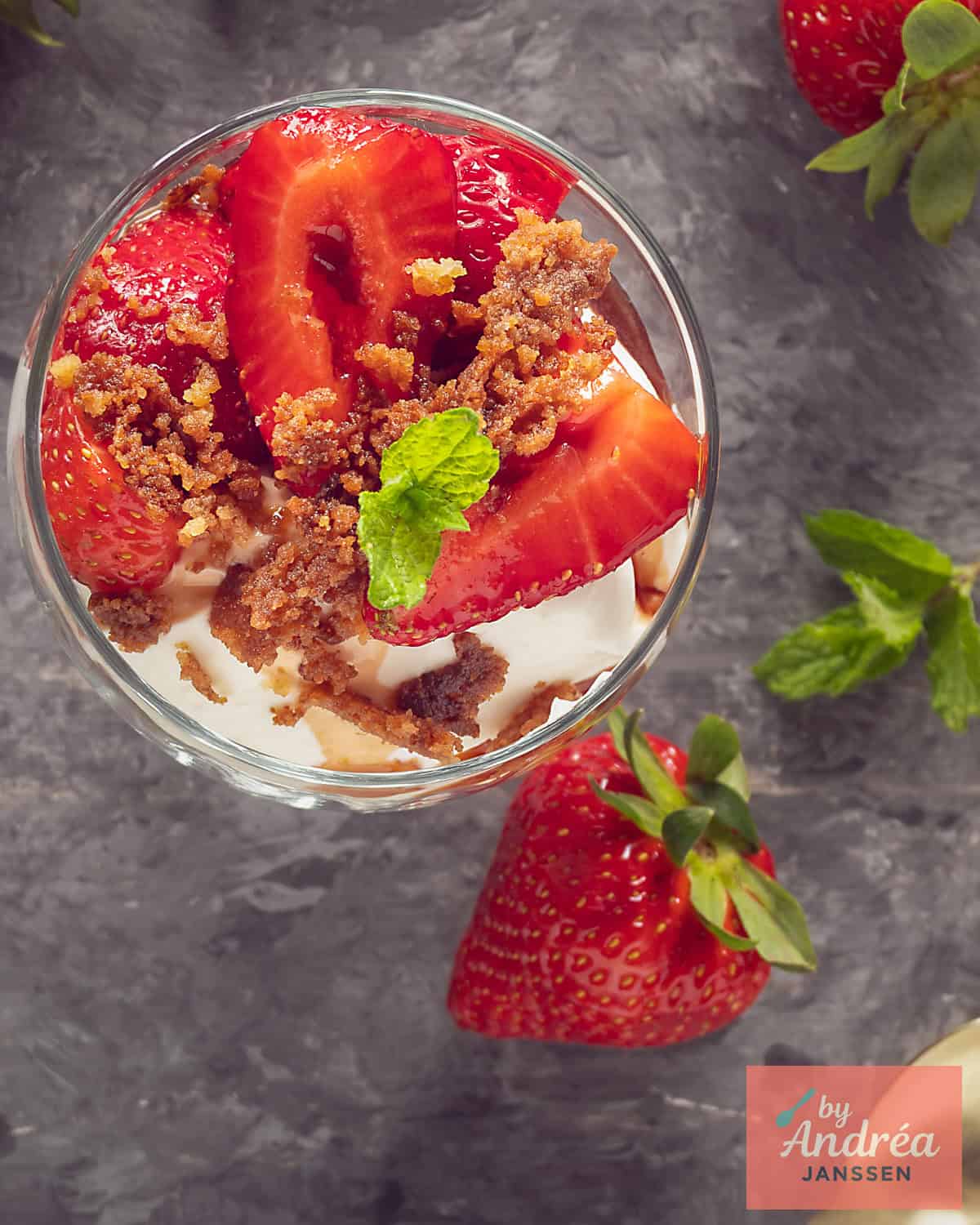 An overhead shot of a glass bowl containing pieces of marinated strawberries, vanilla crumble, and creamy strained yogurt.