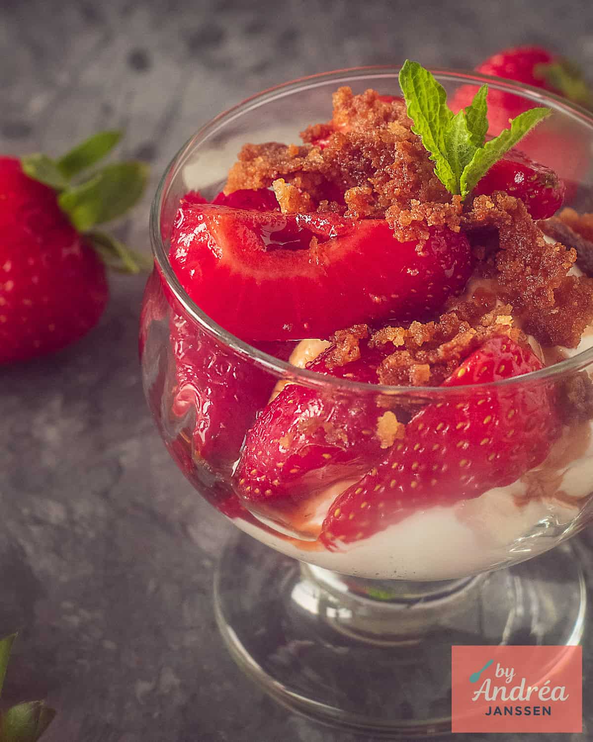Part of a glass with strawberries, vanilla crumble and yoghurt