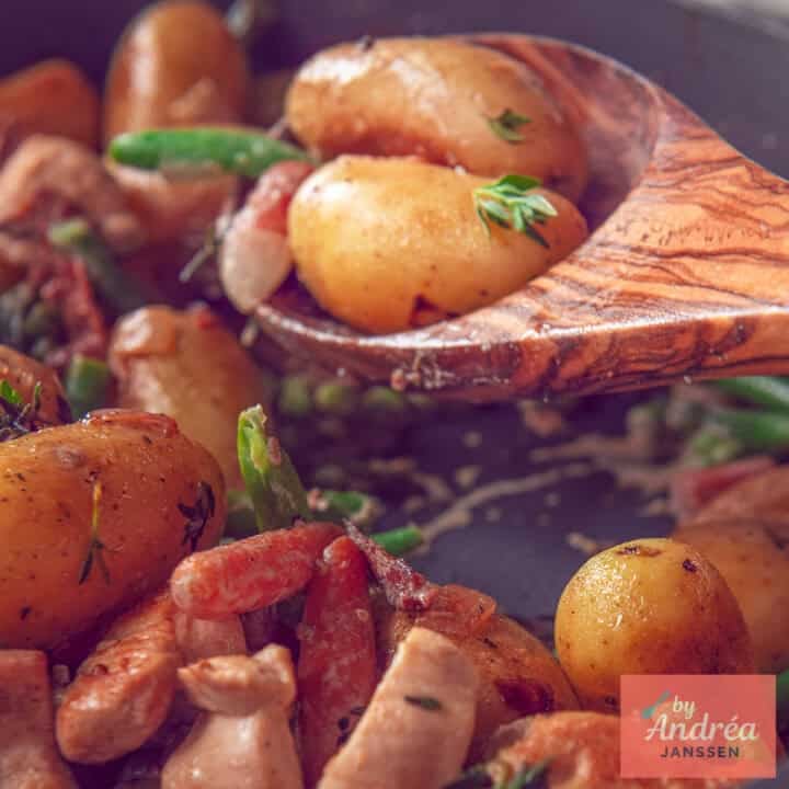 A square photo of a wooden spoon with potatoes, vegetables and chicken