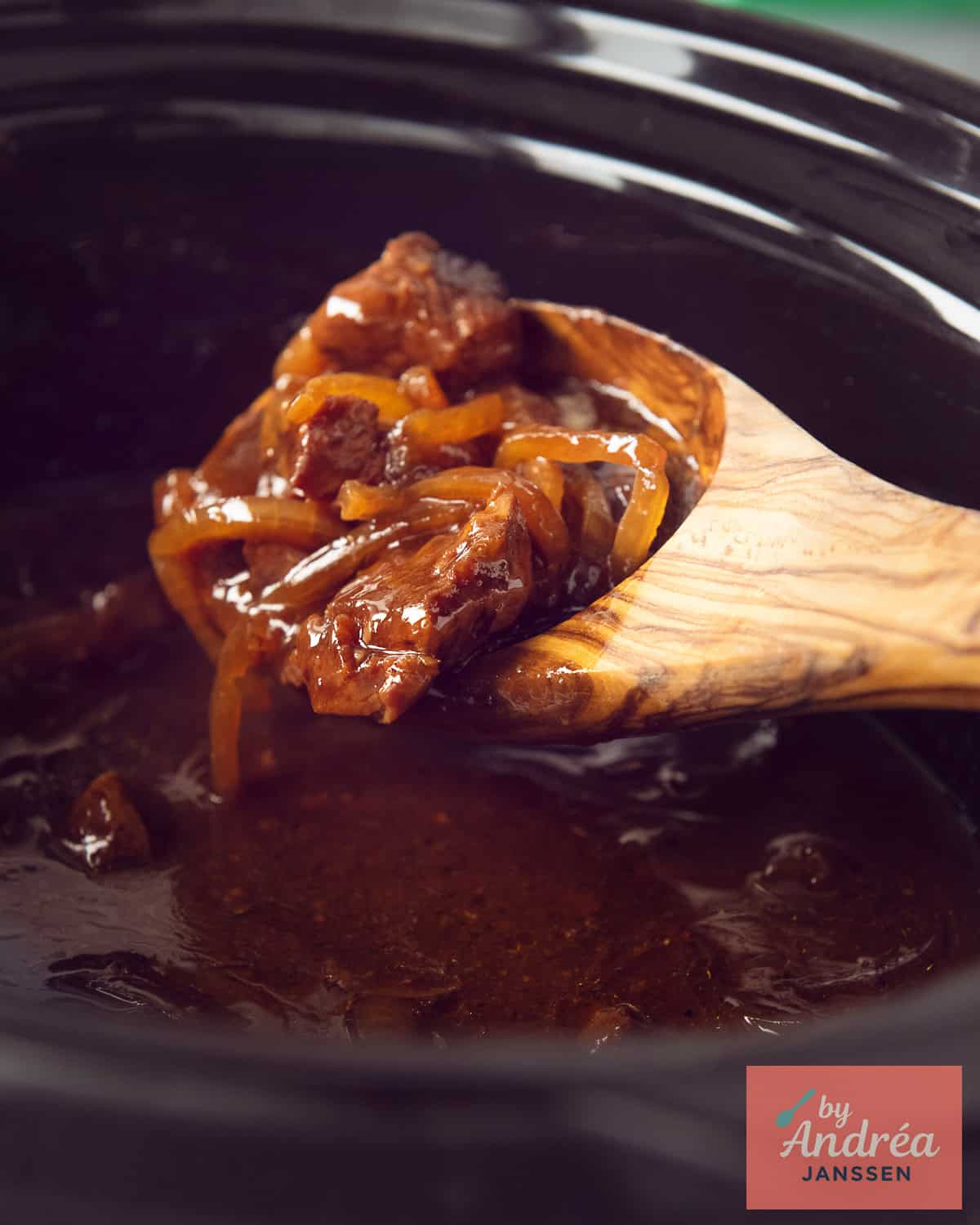 A slow cooker where a wooden spoon scoops stew meat