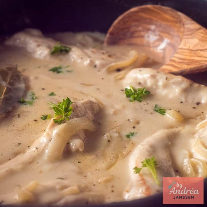 A square photo of a pan of chicken in cream sauce, with onion and white wine.