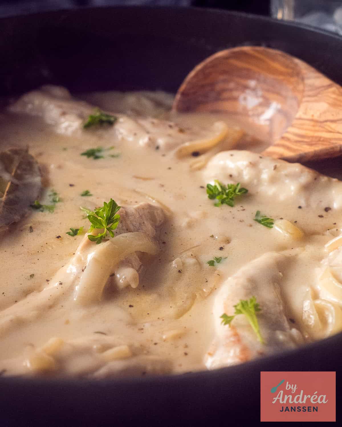 A pan of chicken, cream, onion and thyme with a wooden spoon.