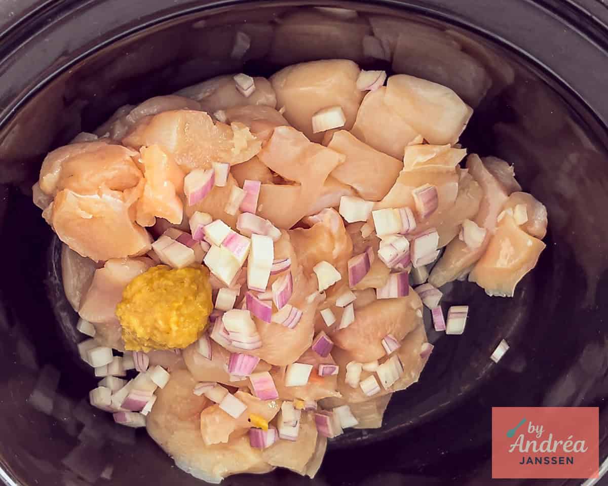 A slow cooker with herbs, onion and garlic and chicken