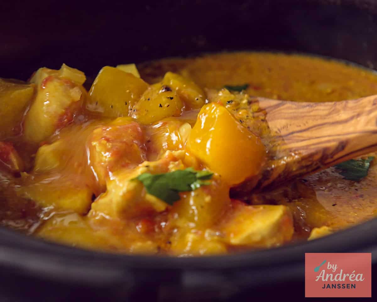 A slow cooker with chicken curry, mango and herbs.