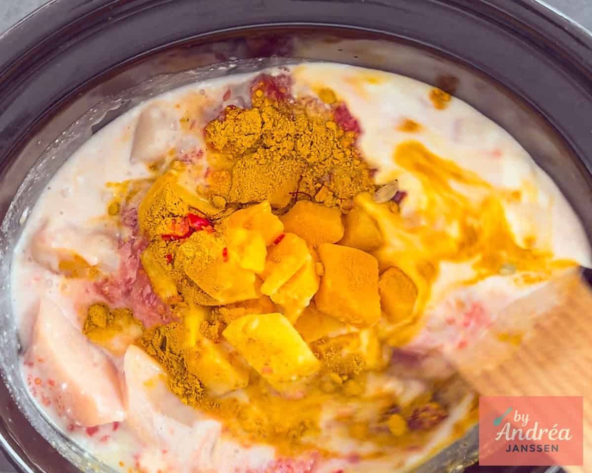 A slow cooker with chicken, herbs, tomatoes, coconut milk and mango